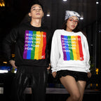 Two young adults model the Custom Hate Has No Home Here Pride Sweatshirt, featuring a rainbow stripe and anti-hate message, embodying inclusivity and LGBTQ+ pride in an urban setting.
