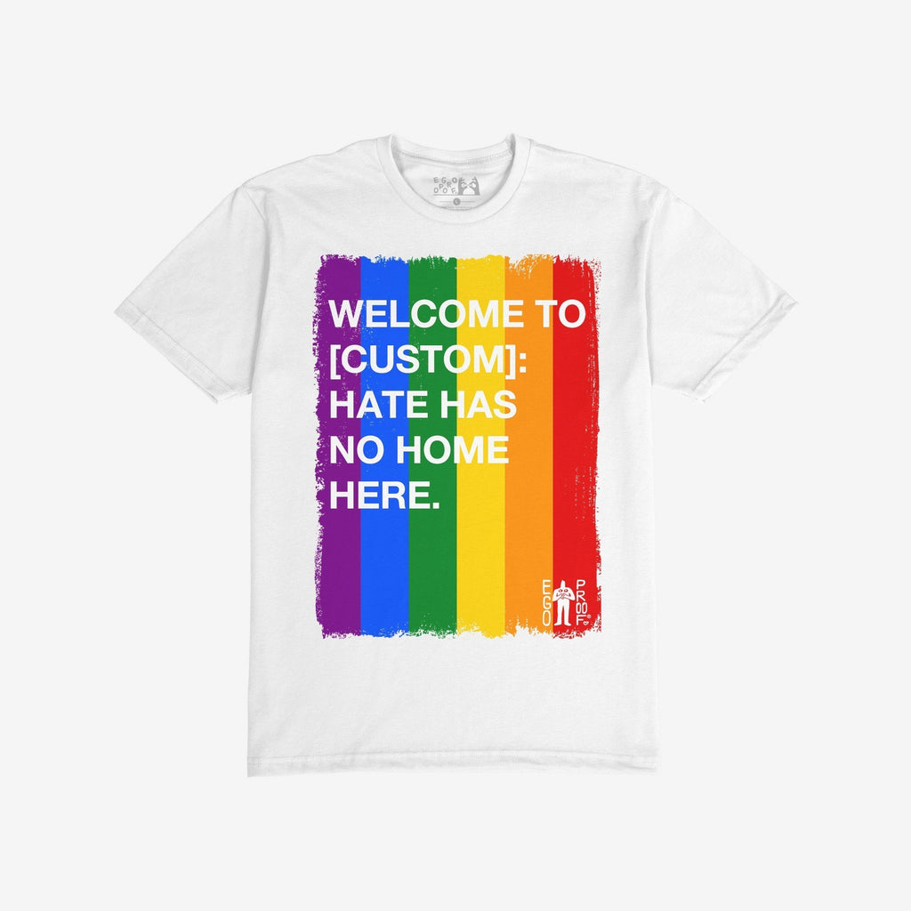 Custom Hate Has No Home Here Pride T-shirt featuring a rainbow brush-stroke panel with customizable location text and bold anti-hate message, embodying unity, inclusion, and pride.