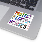 Silver laptop corner with a Protect My LGBTQ+ Homies sticker featuring hand-drawn letters in pride colors, emphasizing equality and allyship. Sticker credit: strangegang.com @_strangegang.