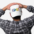 Person wearing a white LGBTQ Rocks Hat with rainbow embroidery and a lightning bolt design on the back, styled with a plaid shirt.