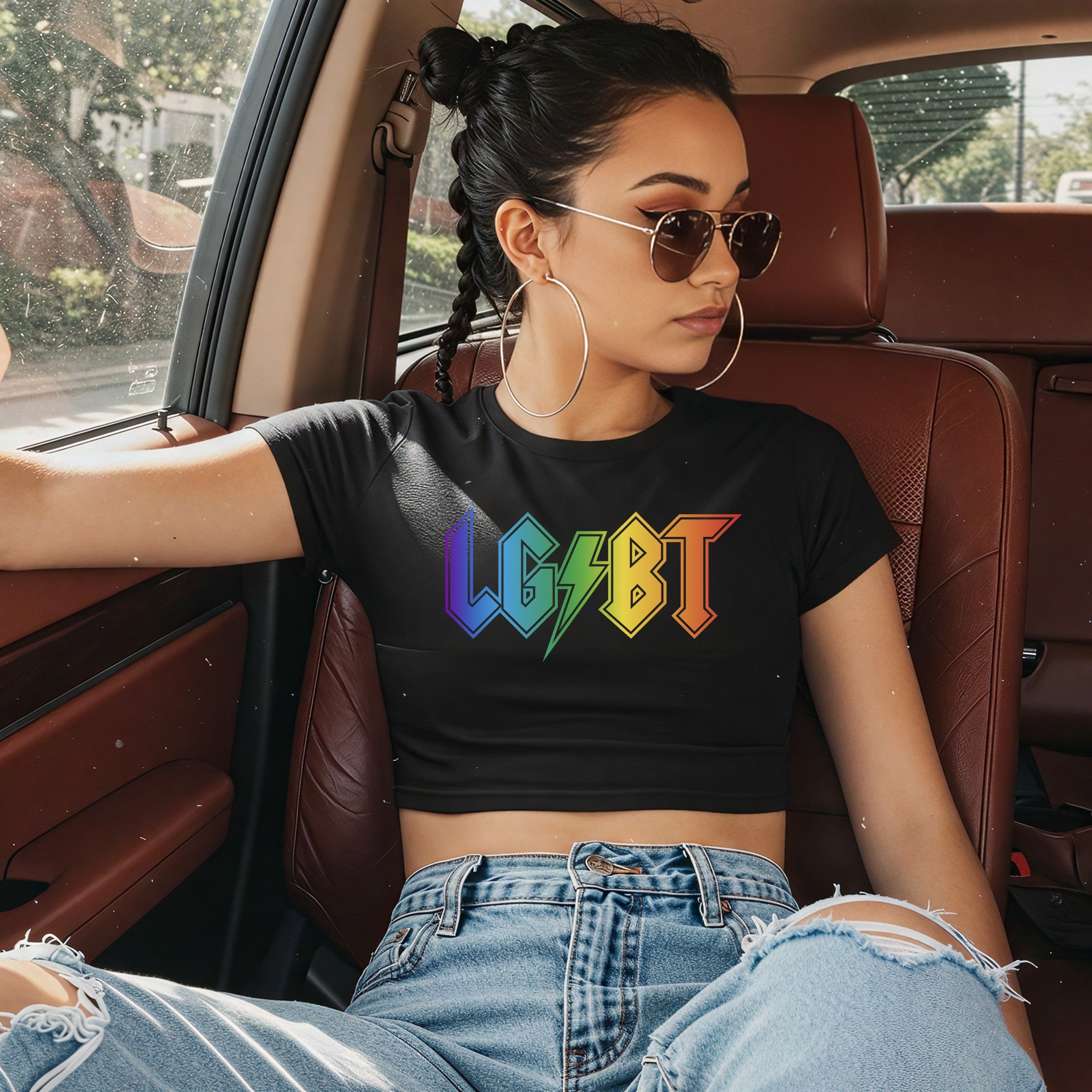 Young person in aviators wearing the LGBTQ Rocks Women's Baby Tee with rainbow-accented LGBT on black, relaxed in a car with reddish-brown leather, embodying bold, unapologetic pride.