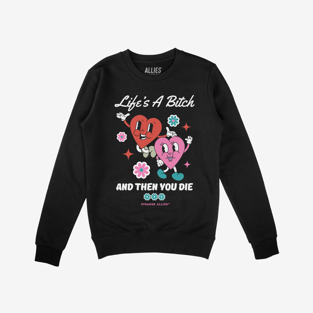 Black crewneck sweatshirt featuring the Life's A Bitch design with two smiling hearts, flowers, and sparkles, encapsulating a humorous yet cynical outlook, aligning with a message of unapologetic realism.