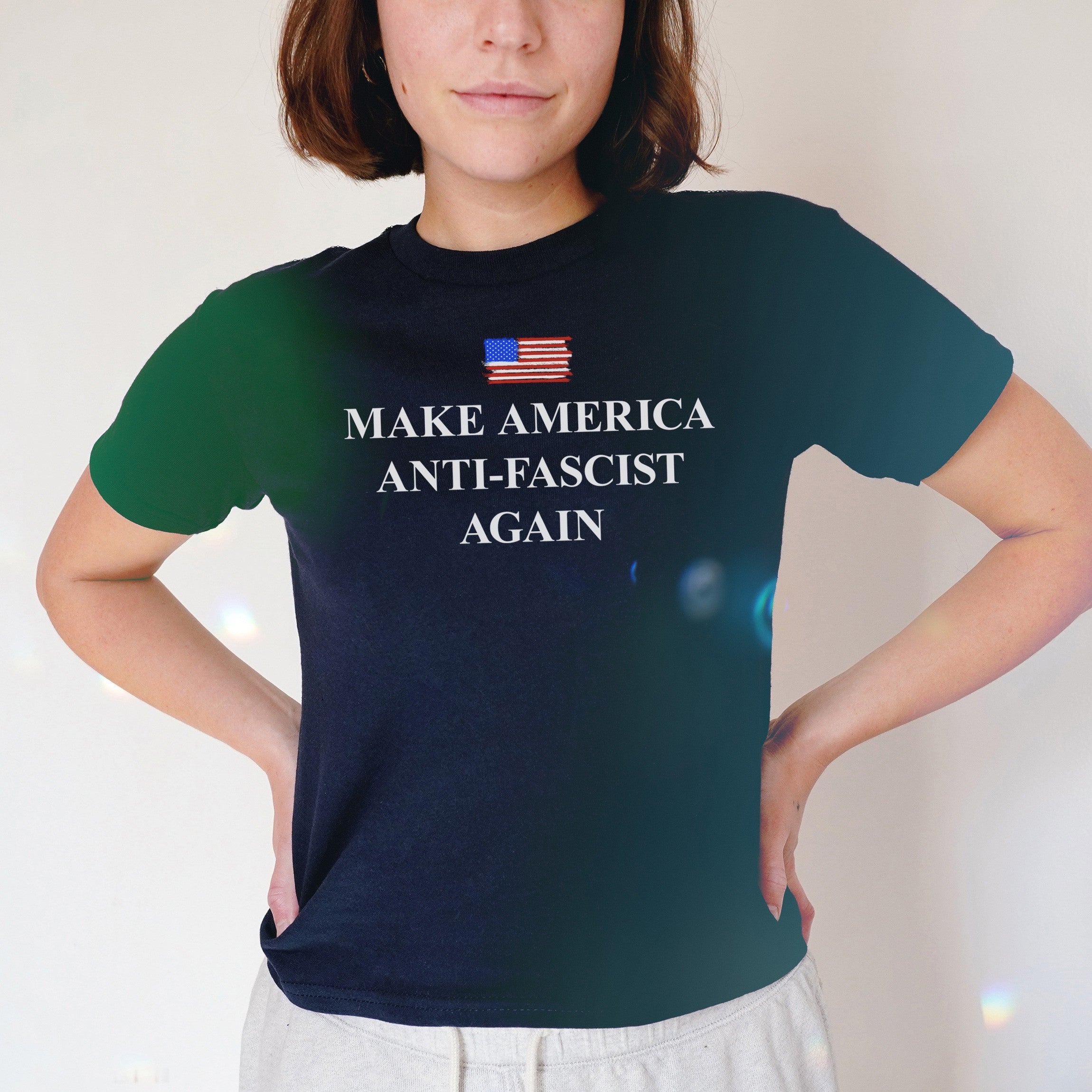 Person wearing the Make America Anti-Fascist Again Women's Baby Tee, featuring a stylized American flag and bold slogan. The tee embodies resistance and retro flair, aligning with anti-fascist and equality-supporting values.
