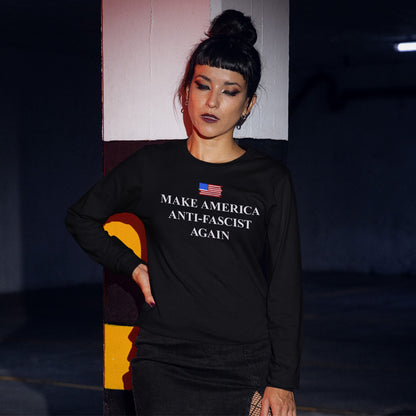 Person in dim parking garage wears Make America Anti-Fascist Again T-shirt with American flag, leaning on a pillar, embodying a bold protest against authoritarianism and promoting equality.
