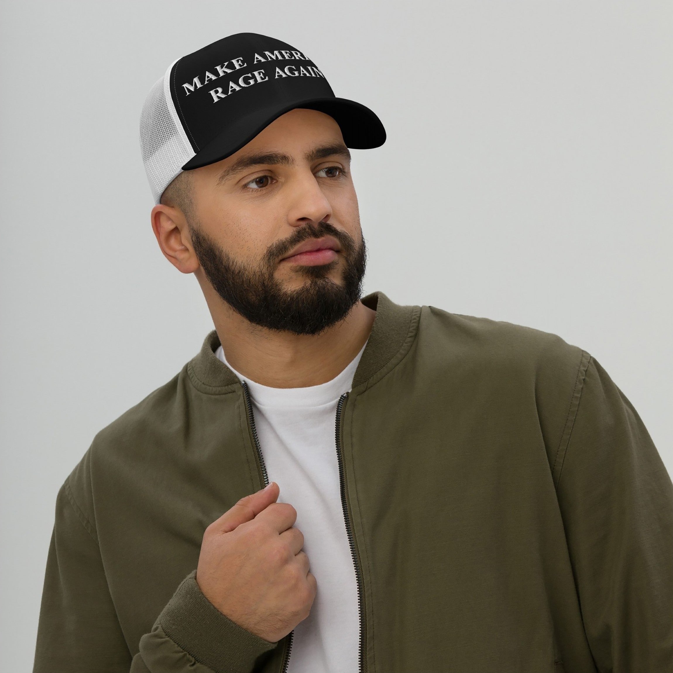 Man wearing Make America Rage Again Hat, a black-and-white trucker cap with bold protest design, paired with an olive-green jacket, embodying anti-fascist sentiments and promoting visible activism.