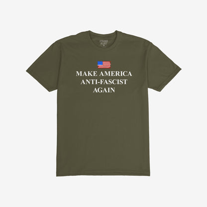 Make America Anti-Fascist Again T-shirt with a small U.S. flag and bold serif slogan, reflecting a stance against authoritarianism, showcasing the message above “STRANGE ALLIES” label inside the collar.