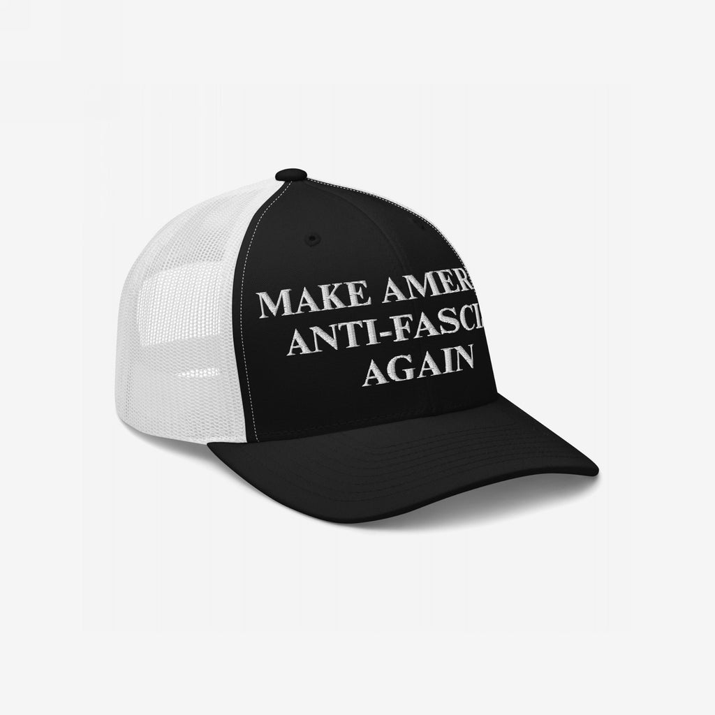 Make America Anti-Fascist Again Hat: A black-and-white trucker cap with a bold embroidered slogan promoting anti-fascism, featuring black front panels and bill with white mesh back panels.