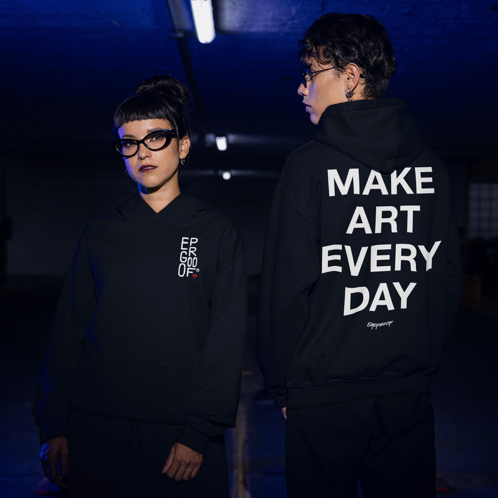 Two people in black hoodies; one facing forward with EGOPROOF logo, the other showing bold Make Art Every Day slogan on the back, embodying creative, expressive style.