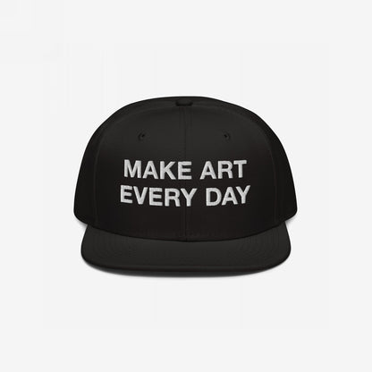 Black flat-brim snapback cap with “MAKE ART EVERY DAY” embroidered in bold white letters on the front. The back features EGOPROOF embroidery, adding a creative touch for committed artists and designers.