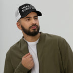 Young bearded man wearing the Make Art Every Day Hat, a black-and-white mesh trucker cap, embodying creativity. The cap features an adjustable closure for comfort, perfect for artists and dreamers.