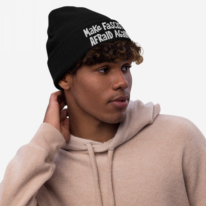 Young man in a pale-beige hoodie wears a black Make Fascists Afraid Again knit beanie, featuring bold, hand-drawn lettering, embodying a spirit of unapologetic resistance.