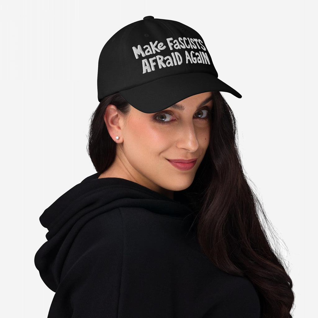 Woman in a black hoodie and cap with Make Fascists Afraid Again embroidered, embodying protest and resistance.