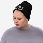 A young adult wears the Make Fascists Afraid Again hat, showcasing its bold slogan in raw, hand-drawn embroidery. The black knit beanie complements their understated gray top, embodying everyday resistance.