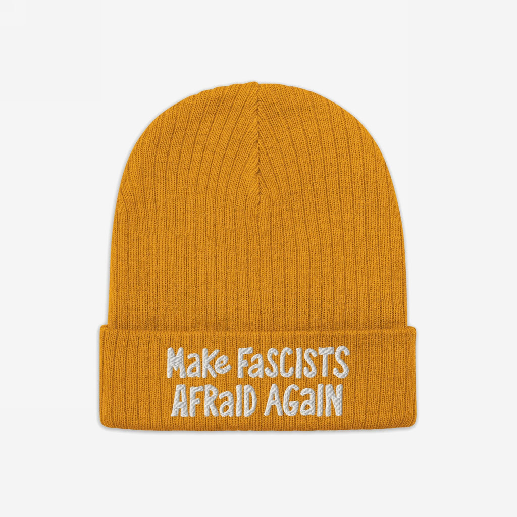 The Make Fascists Afraid Again Hat features a mustard-yellow knit with white embroidered slogan on its cuff, embodying defiance and supporting equality. Profits aid ACLU.