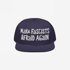 Dark-blue flat-brim cap with white embroidery reading “Make Fascists Afraid Again.” Features raw, hand-drawn style for everyday resistance; proceeds support the ACLU.