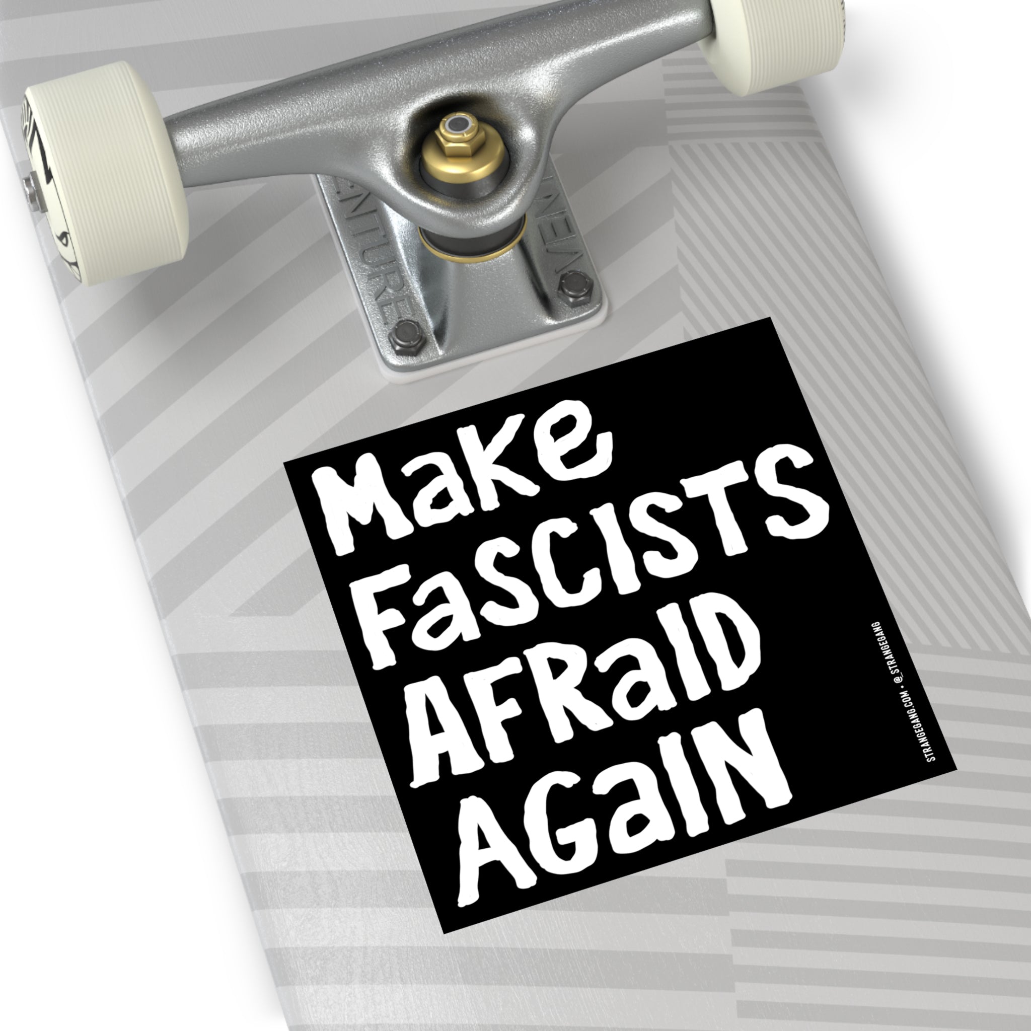 The underside of a skateboard deck displays the Make Fascists Afraid Again sticker, featuring hand-lettered block text and a metal truck with white wheels, symbolizing defiance against authoritarianism.