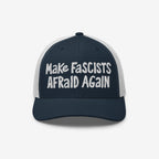 Make Fascists Afraid Again Hat features navy front and bill with white mesh back. Bold white embroidery showcases defiance, perfect for protests or casual wear supporting equality and resisting fascism.