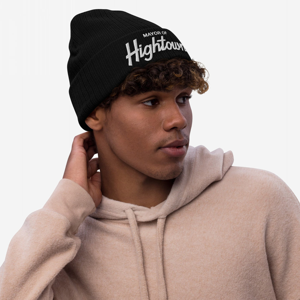 Young person in a light-beige hoodie wears the Mayor Of Hightown beanie, featuring bold embroidery, capturing the playful and rebellious spirit of cannabis culture against a white backdrop.