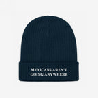 Dark navy-blue knit beanie with “MEXICANS AREN’T GOING ANYWHERE” embroidered in white, embodying pride and resistance against racism and nationalism.