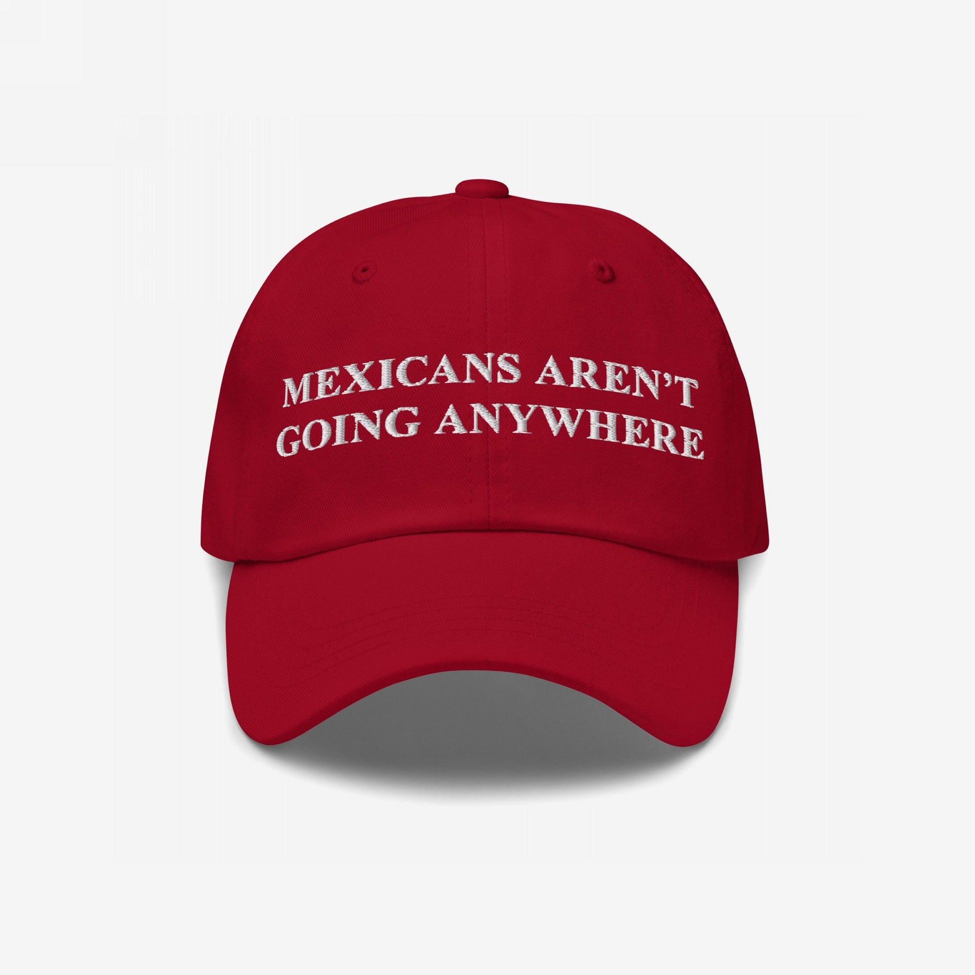 Red baseball cap with white embroidered text: MEXICANS AREN’T GOING ANYWHERE. The Mexicans Aren’t Going Anywhere Hat represents resilience and pride, challenging racism and supporting immigrant rights.