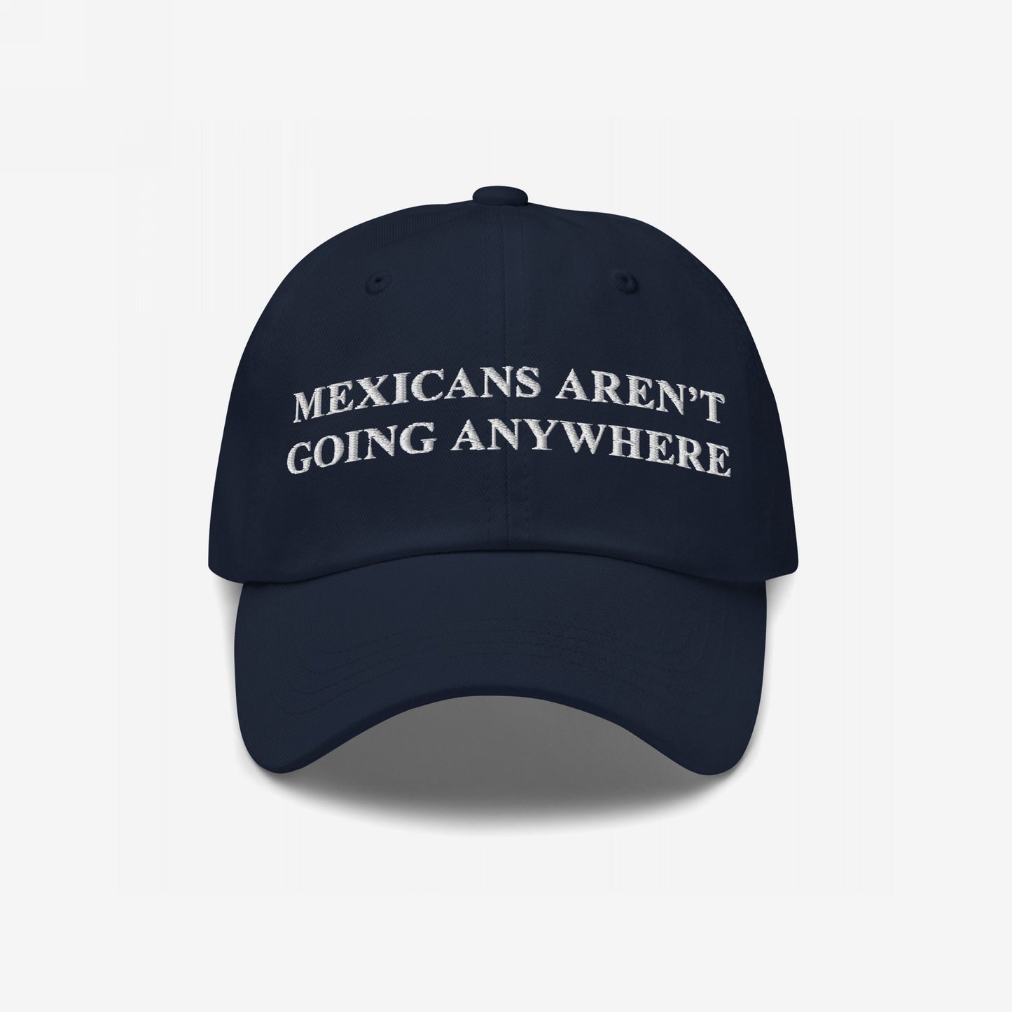 Dark-navy cap with white embroidery reads “MEXICANS AREN’T GOING ANYWHERE,” symbolizing pride and resistance, crafted to challenge racism and support immigrant rights.