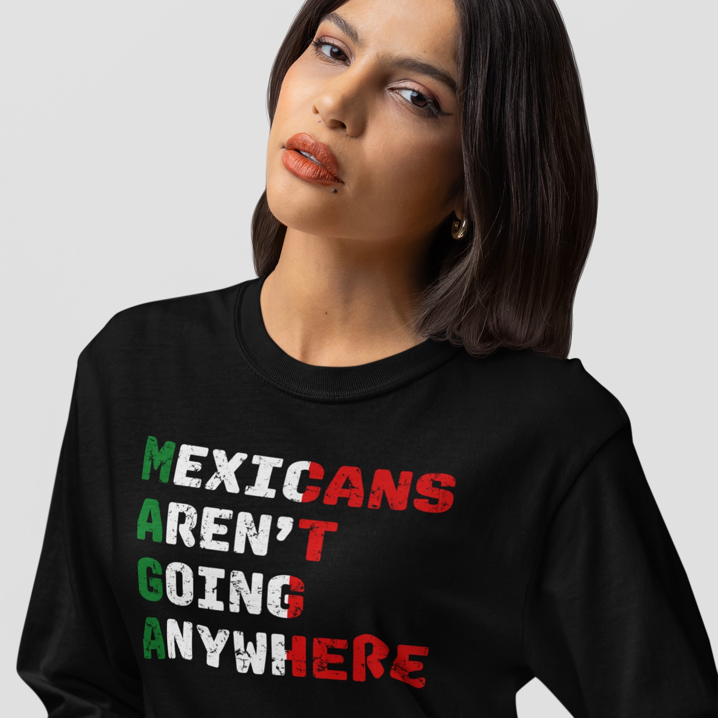 A woman models the Mexicans Aren’t Going Anywhere Shirt, a black sweatshirt with a bold slogan in Mexican flag colors, symbolizing resilience and pride against discrimination.