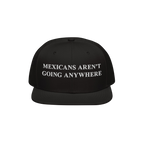 Black snapback hat featuring bold white embroidery reading “Mexicans Aren’t Going Anywhere,” symbolizing pride and resi
