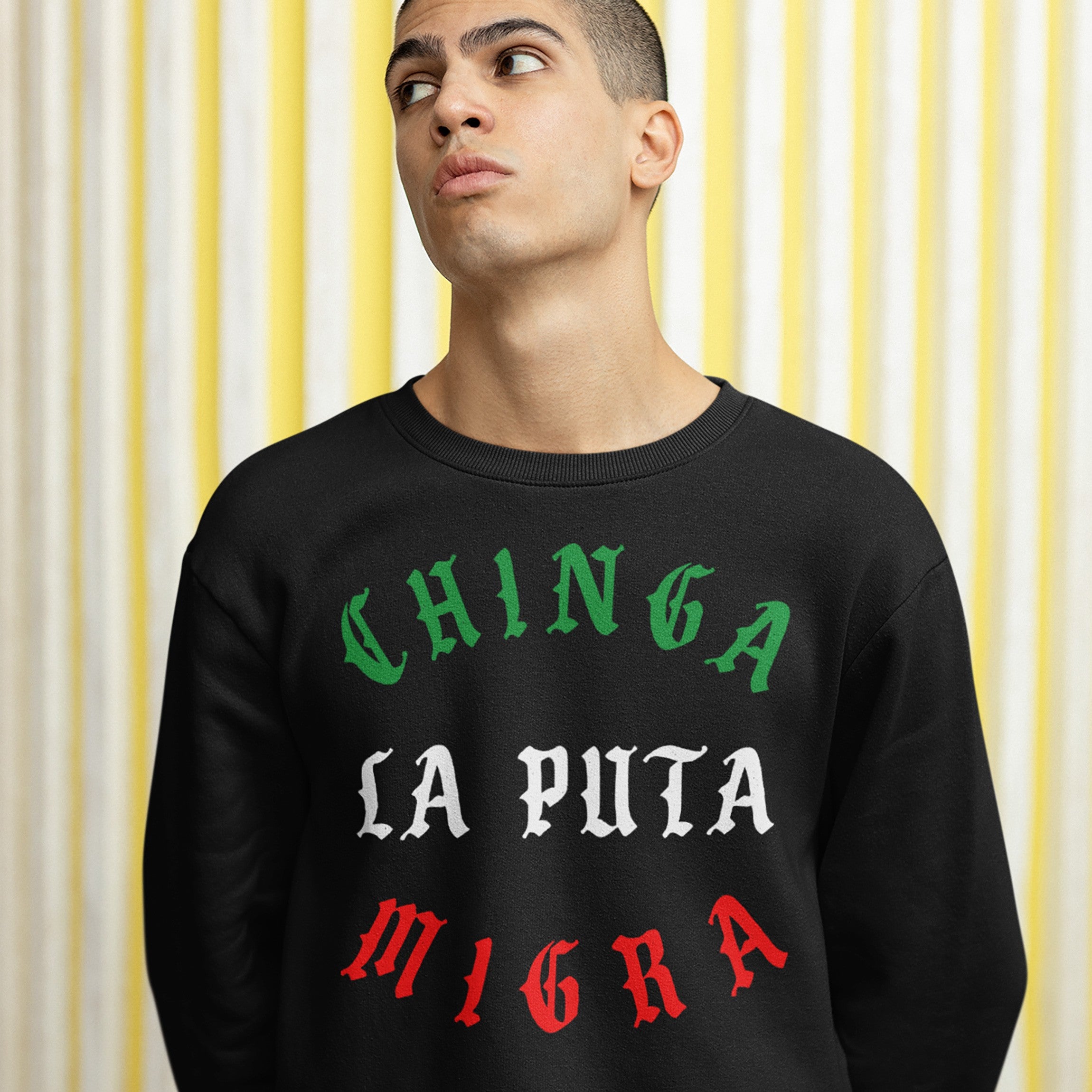 Young man wearing a Chinga La Migra Mexico Hoodie & Sweatshirt, featuring bold protest text in blackletter style, embodying a powerful anti-ICE message, standing against a striped background.