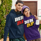 Two young adults indoors wearing Minnesota As Fuck Anti-Fascist Hoodies; left in navy blue, right in purple with matching beanie, symbolizing equality and anti-fascism. Both smile softly, one holding a mug.
