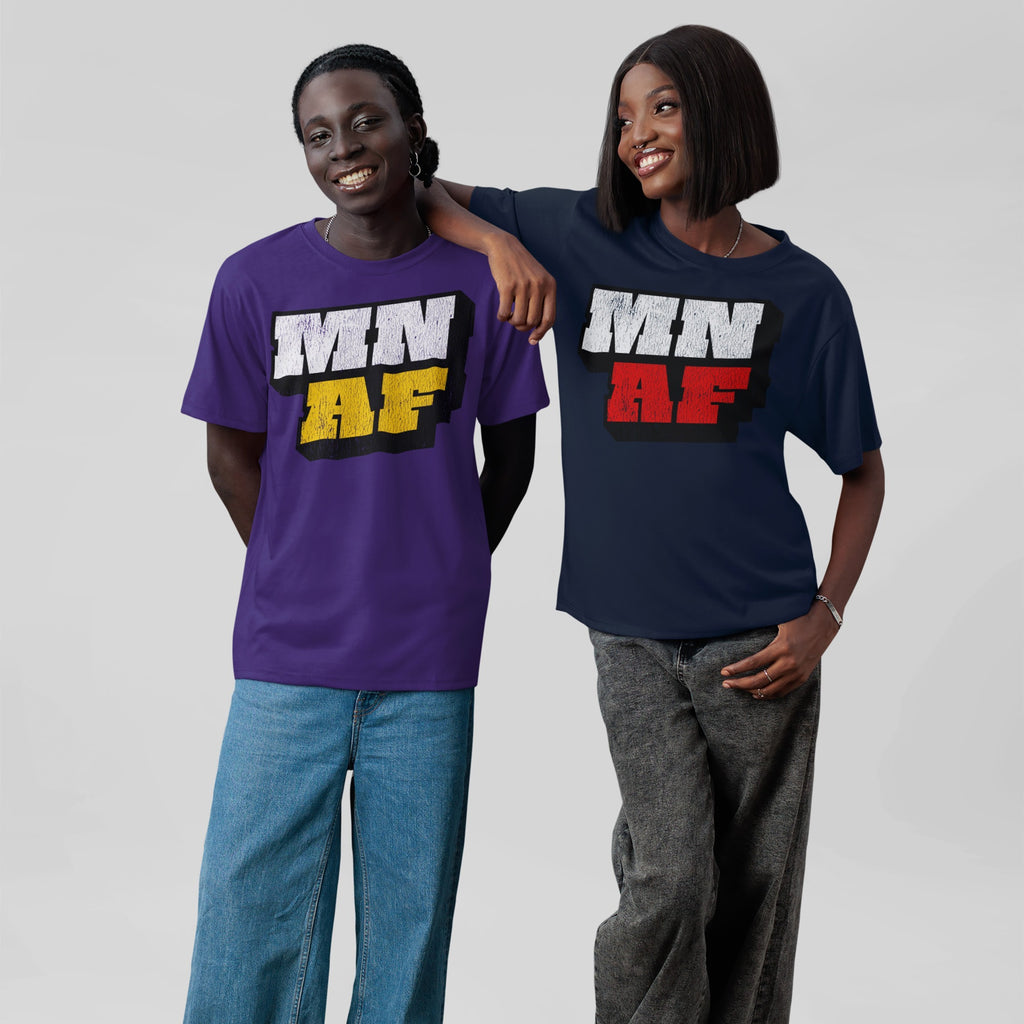 Two individuals wearing Minnesota As Fuck Anti-Fascist T-shirts, one in purple and the other in navy, both smiling. The shirts feature bold block lettering, conveying a message of defiance and solidarity.