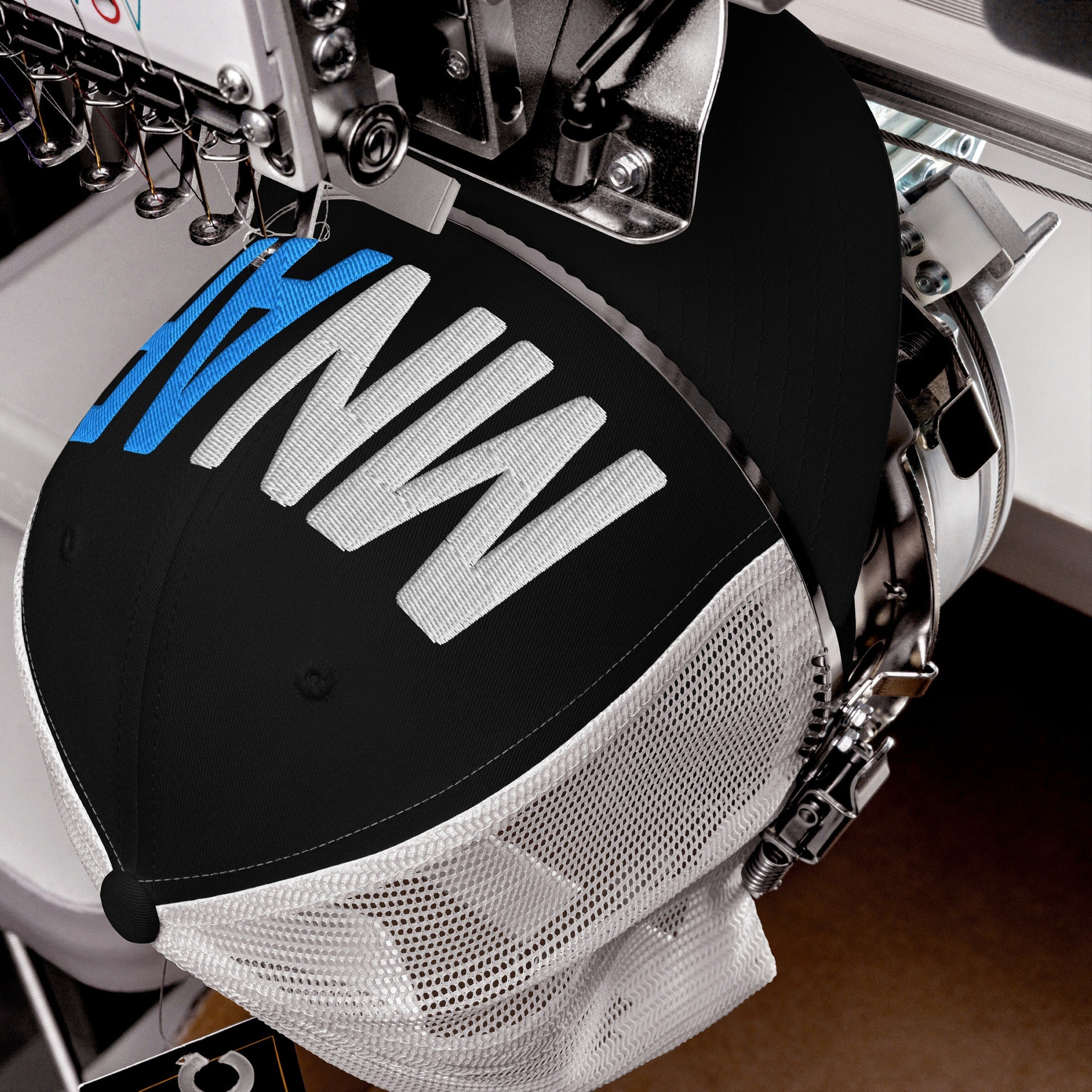 Industrial embroidery machine stitching MN AF on a black trucker cap, embodying the Minnesota As Fuck Anti-Fascist Hat's pro-equality and anti-fascism message with white and blue threads.