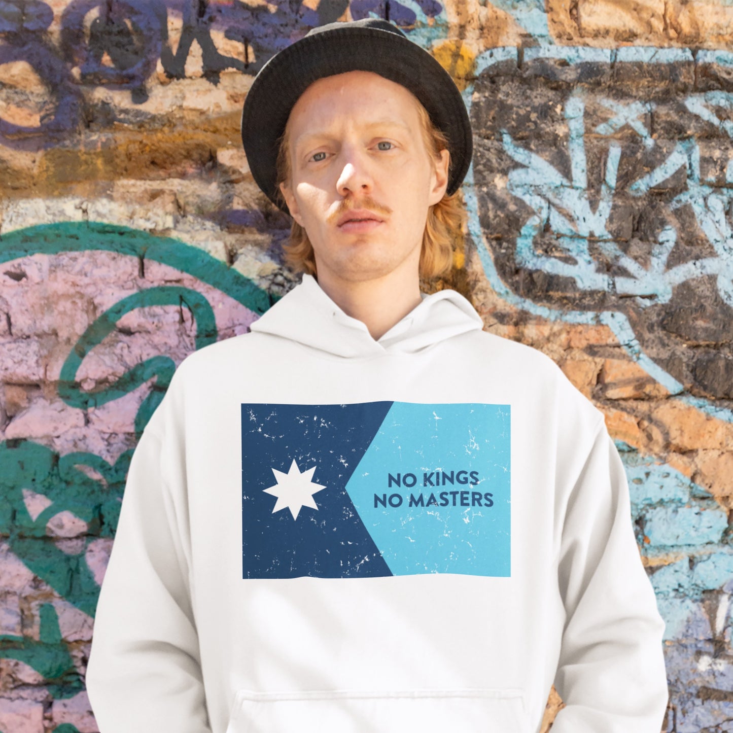 Person in a white hoodie featuring the Minnesota No Kings Flag Shirt design with a two-tone blue graphic, eight-pointed star, and the words NO KINGS NO MASTERS, embodying a spirit of resistance.
