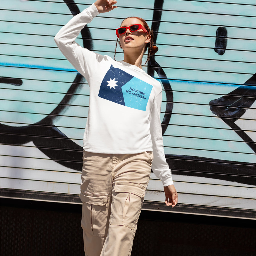Person wearing the Minnesota No Kings No Masters Flag Shirt, featuring a two-tone blue graphic and slogan, stands before a graffiti backdrop, embodying a rebellious streetwear style against authoritarianism.