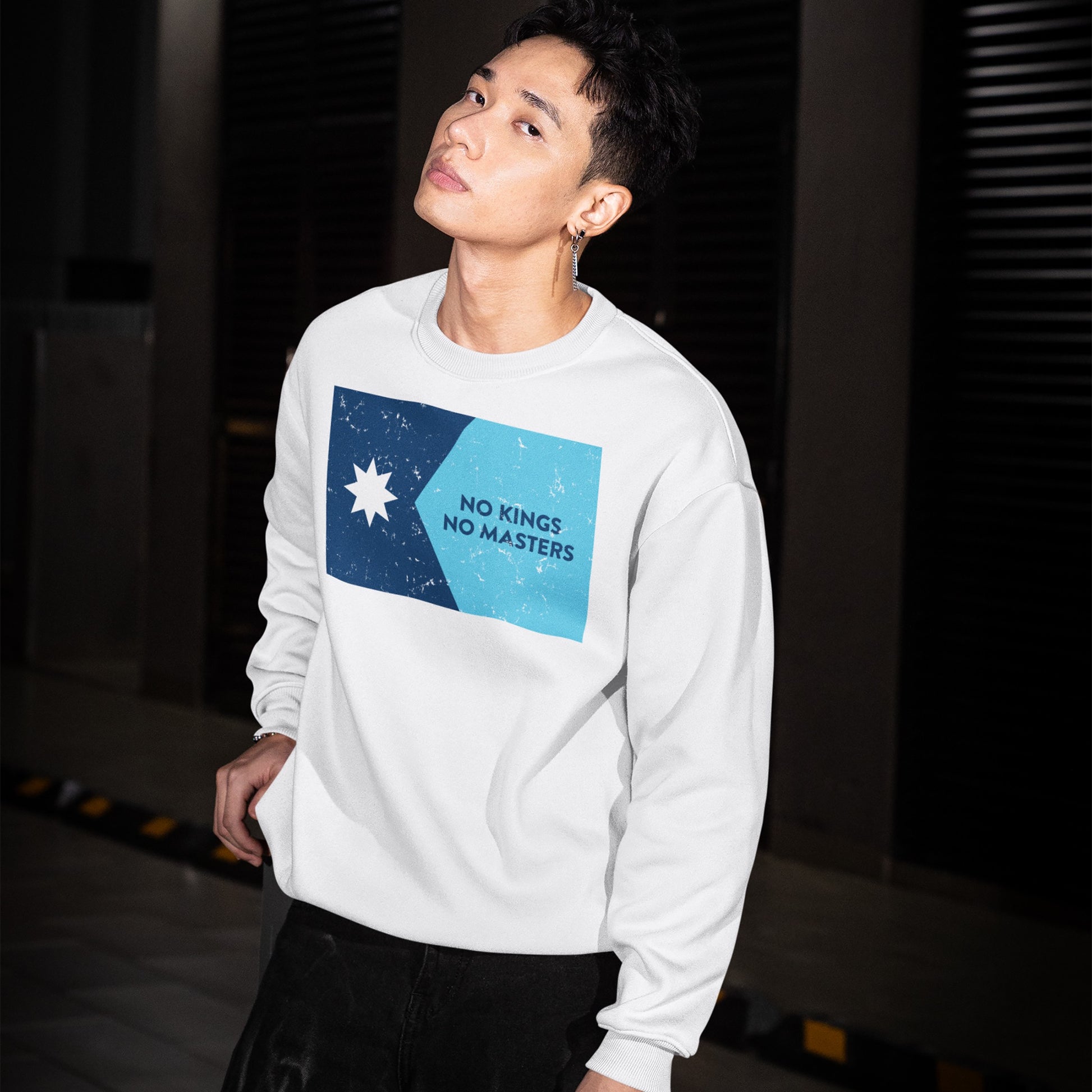 Young man models the Minnesota No Kings Flag Hoodie & Sweatshirt in an urban setting, showcasing the bold two-tone blue graphic with empowering NO KINGS NO MASTERS text and a white star design.