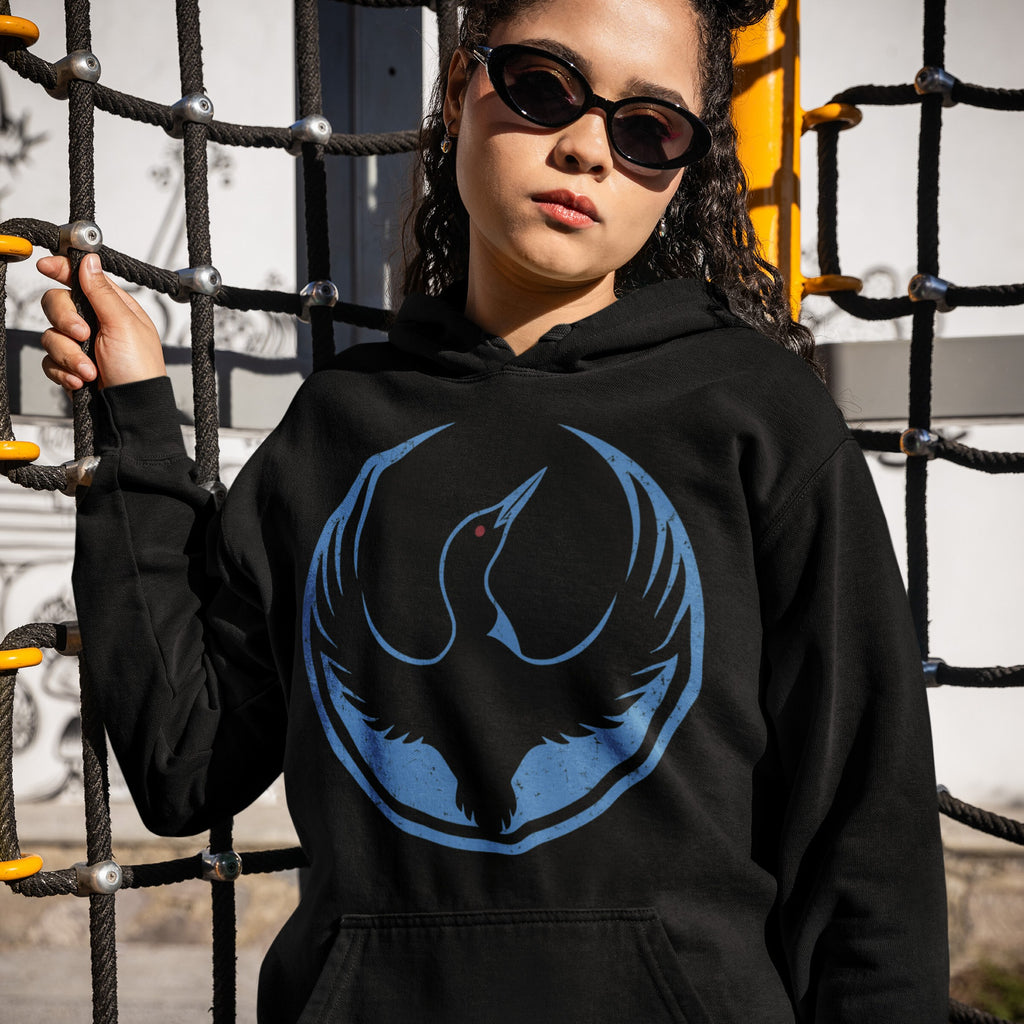 Young woman outdoors wearing Minnesota Rebel Alliance Hoodie with blue bird logo, gripping a climbing structure. This hoodie embodies support for immigrant rights and equality, reflecting a bold, activist spirit.