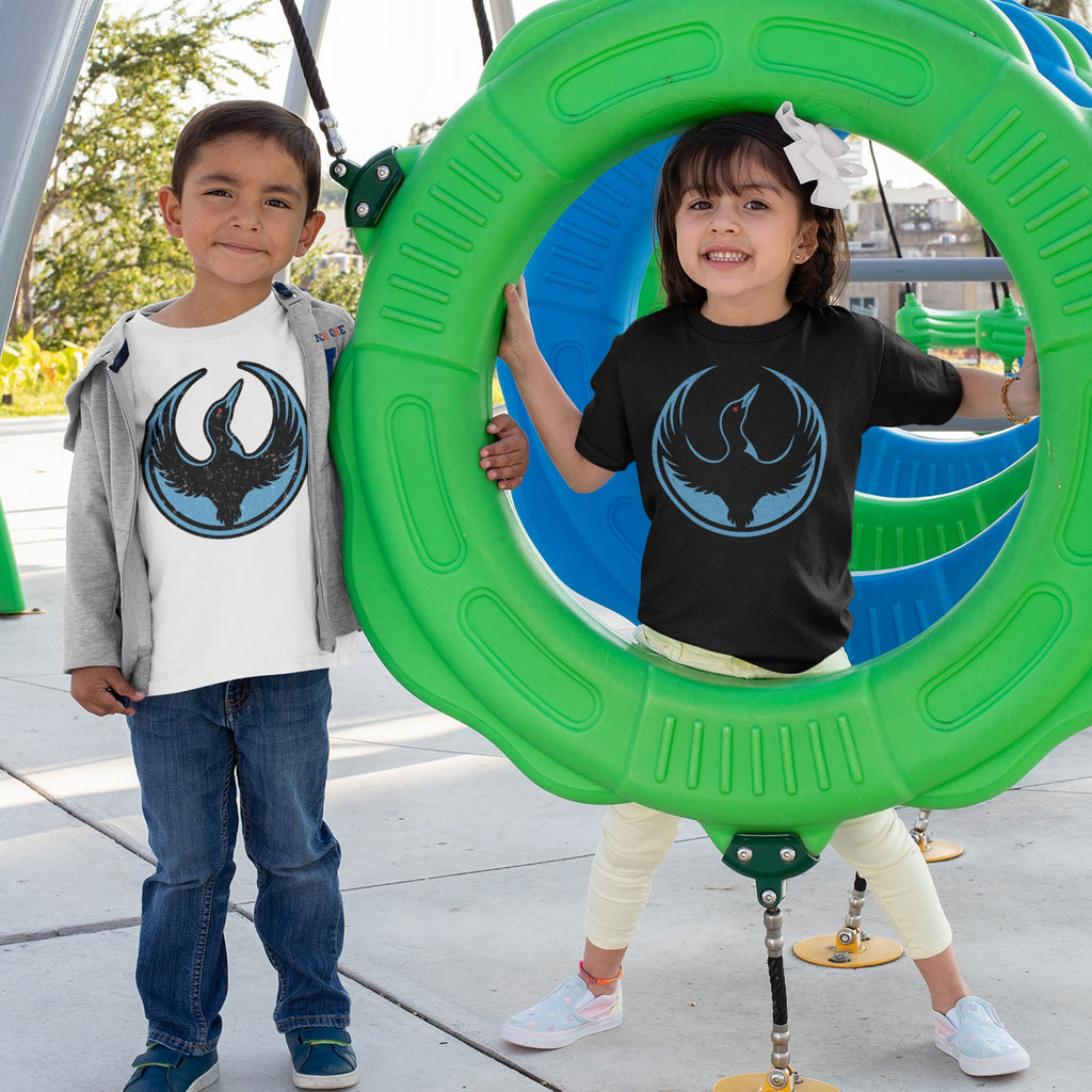 Two children wearing Minnesota Rebel Alliance T-shirts with a loon emblem play on a green playground ring, smiling brightly. The design reflects bold, non-neutral activism through fashion.