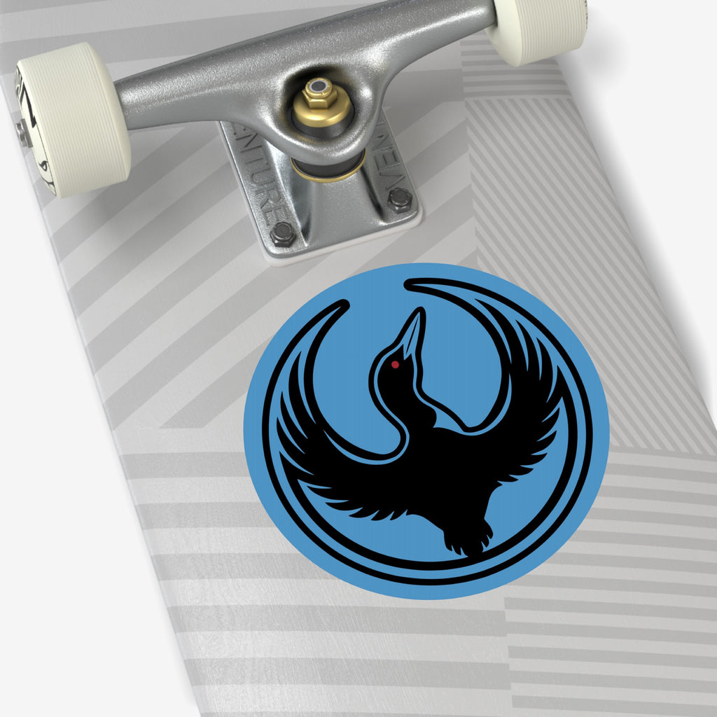 Close-up of a skateboard deck underside featuring a silver “Venture” truck, off-white wheel, and the Minnesota Rebel Alliance Sticker—a blue circle with a black bird, emphasizing anti-fascism and immigrant rights.