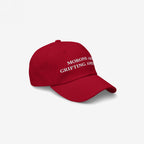 Angled view of the red dad hat showing the white "Morons Are Grifting America" embroidery — a satirical, anti-MAGA twist on the classic right-wing look.