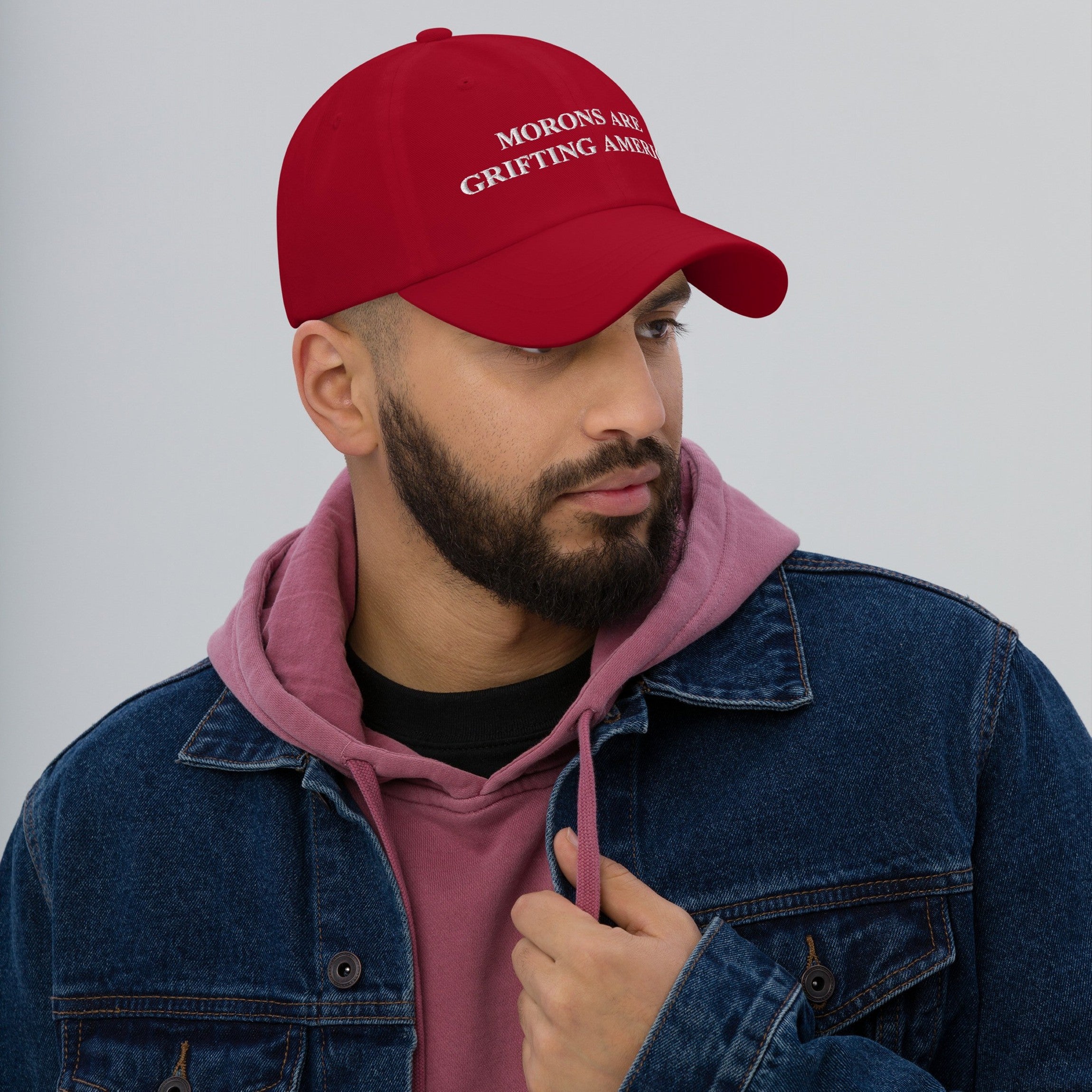 Man wearing the red "Morons Are Grifting America" dad hat styled like a MAGA cap but delivering a progressive, anti-MAGA punch in a bold red protest fit.