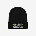 The No Kings No Masters Hat features a black rib-knit design with a fold-over cuff, showcasing the slogan “NO KINGS NO MASTERS” in white, flanked by yellow crown motifs.