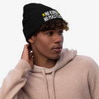 Young man in a light-beige hoodie wearing the No Kings No Masters Hat, a black knit beanie with NO KINGS NO MASTERS embroidered in white and yellow, embodying a rebellious spirit.