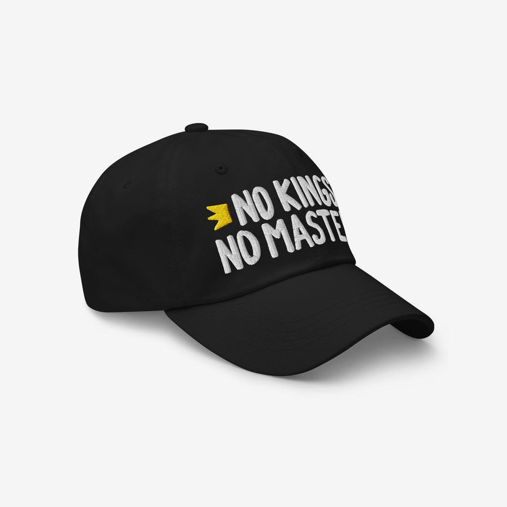 Black cap with white embroidered text NO KINGS NO MASTERS and a yellow crown motif. Showcasing defiance and individuality, it's ideal for those challenging authority and supporting equality.