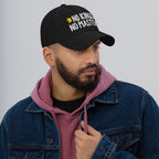 Young man in a blue denim jacket and dusty rose hoodie wears the No Kings No Masters Hat, featuring white embroidered text and yellow arrows, symbolizing rebellion and independence.