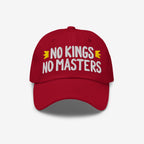 No Kings No Masters Hat: A red unstructured cap with “NO KINGS NO MASTERS” in bold white embroidery, flanked by yellow motifs, representing rebellion and individuality.