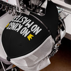 The No Kings No Masters Hat features bold embroidery on a black-and-white trucker cap, picturing an empowering message with arrow accents, captured mid-stitch in an industrial embroidery machine.