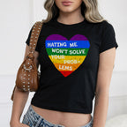 No LGBTQ Hate Women's Baby Tee featuring a rainbow-striped heart with the message “Hating me won’t solve your problems.” Paired with a studded shoulder bag and light-wash jeans.