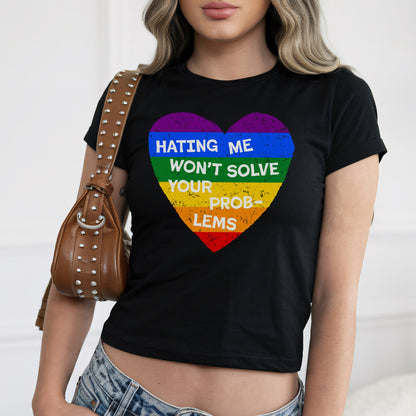 No LGBTQ Hate Women's Baby Tee featuring a rainbow-striped heart with the message “Hating me won’t solve your problems.” Paired with a studded shoulder bag and light-wash jeans.