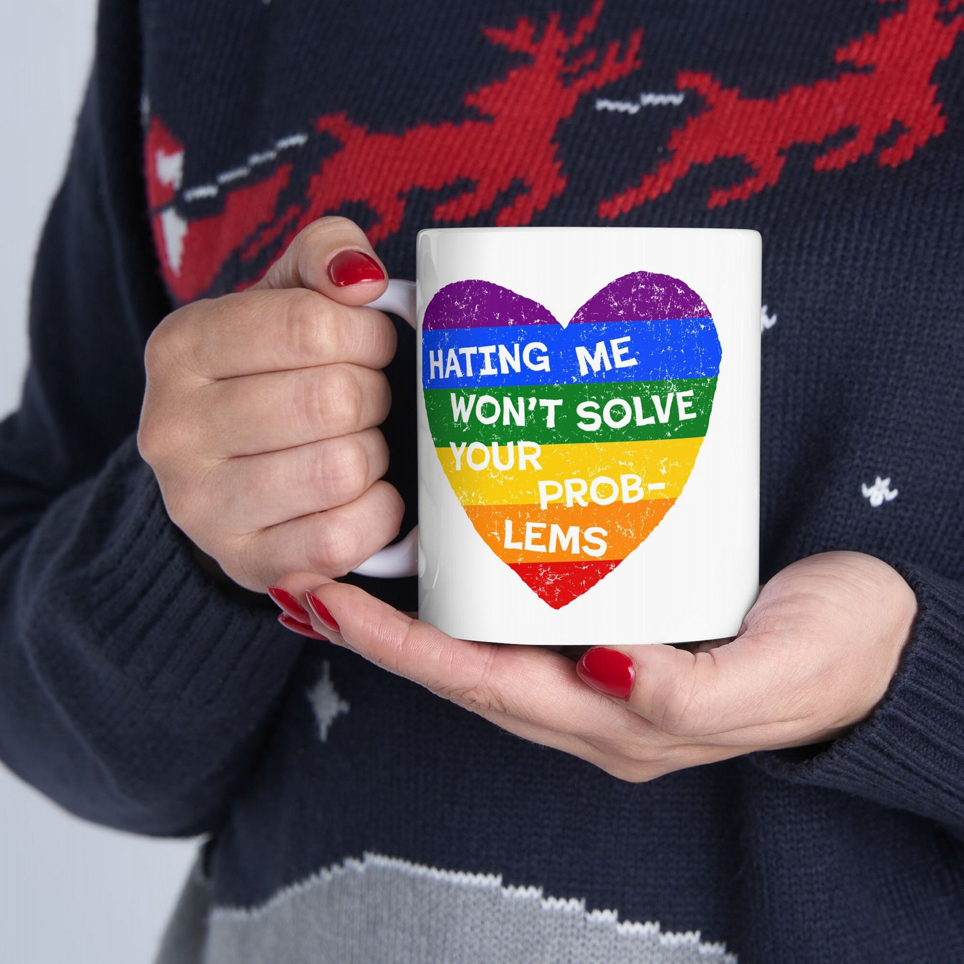 Person holding No LGBTQ Hate Mug with rainbow heart and the message “HATING ME WON’T SOLVE YOUR PROBLEMS,” showcasing pride and defiance. Red nails and dark sweater visible.