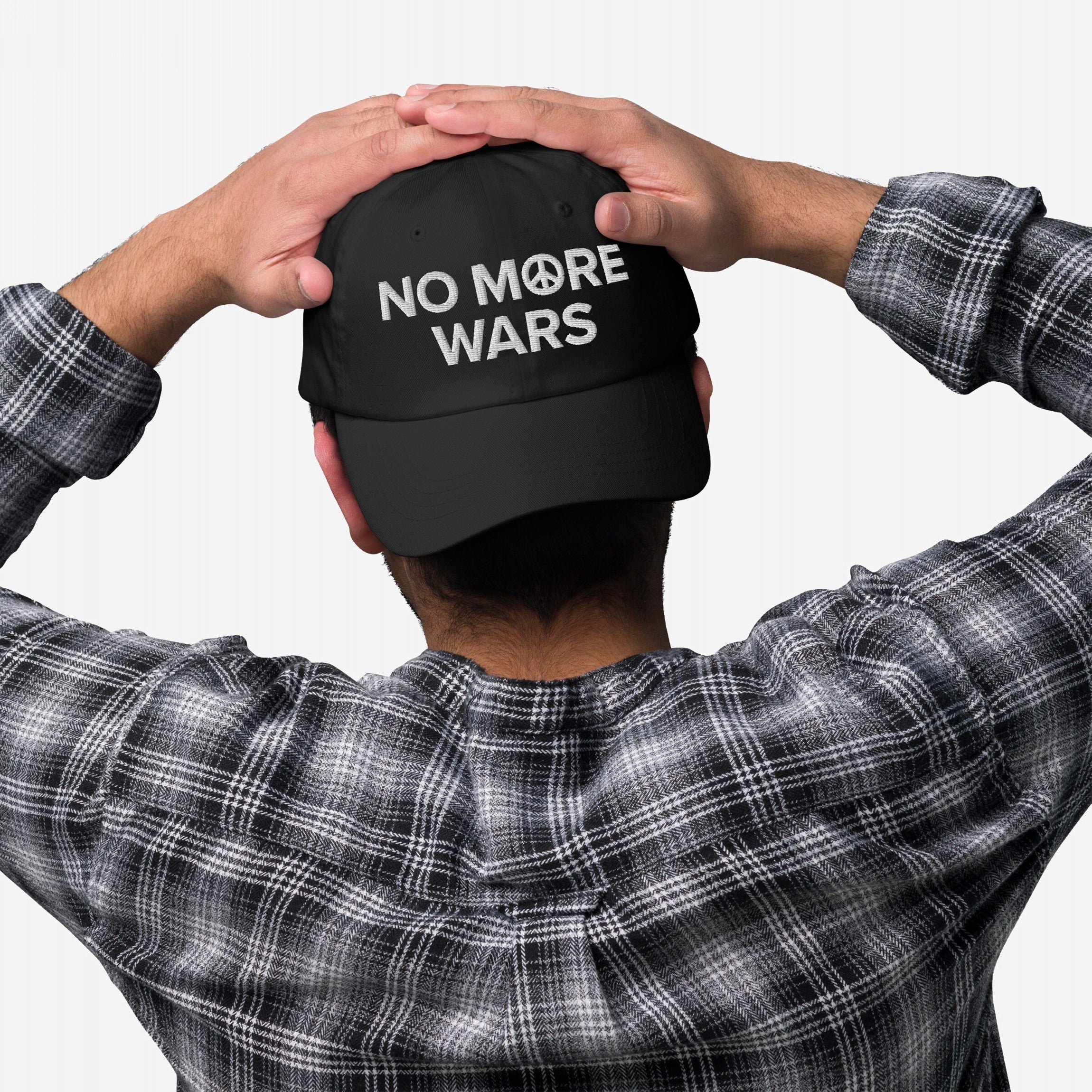 Person wearing No More Wars Hat with peace symbol, hands on head. The cap's bold message opposes war, aligning with the store's ethos of peace and equality.