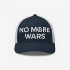 No More Wars Hat featuring navy-blue front, white mesh back, with NO MORE WARS embroidered, peace symbol as the O, promoting peace and resistance against war profiteering.